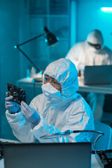 Poster - Young female in protective coveralls holding motherboard while checking it before repairing