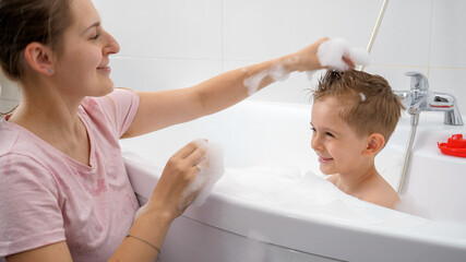 Wall Mural - Happy smiling mother making stylish haircut to her son washing in bathroom. Concept of hygine, children development and fun at home