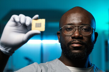 Poster - Young serious man of African ethnicity holding microchip in gloved hand while standing in front of camera