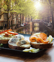Amsterdam City With Fishplate (salomon And Codfish Sandwiches) Against Tourboat On Canal In Netherlands