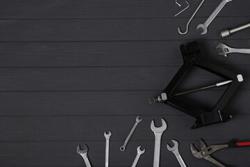 Canvas Print - Car scissor jack and wrench set on black wooden surface, flat lay. Space for text