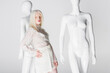 Stylish albino woman with closed eyes standing near mannequins isolated on white.