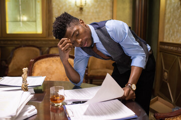 Poster - Young serious African lawyer in suit bending over documents on table while reading one of them before meeting
