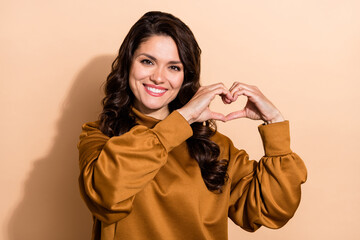 Poster - Portrait of attractive cheerful cute wavy-haired woman showing heart sign 14 February isolated over beige pastel color background