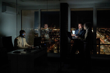 Wall Mural - Group of young intercultural co-workers computing in large openspace office at night