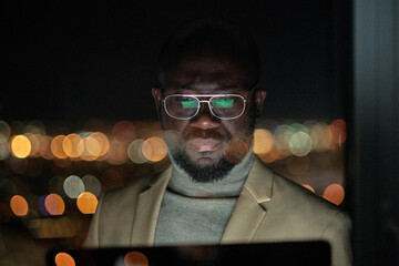 Poster - Serious African businessman in eyeglasses looking at computer screen while working late in the night