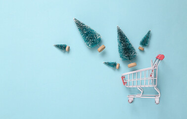 Wall Mural - Shopping cart with mini Christmas trees on a blue background. Top view