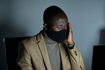 Poster - Tired African businessman with headache touching head while working late in the office