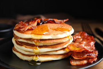 Delicious pancakes with maple syrup and fried bacon on plate, closeup