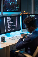 Poster - Busy young programmer of African ethnicity looking at wristwatch while working late in the evening in office