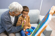 © Dragana Gordic - Grandmother spending happy time with grandson. Woman assisting young boy in painting on canvas. Happy senior woman looking at her grandson painting and smiling at him