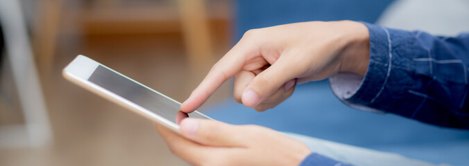 Canvas Print - Closeup hand of young attractive asian man resting using browsing tablet computer on sofa at home, happy male sitting on couch relax read digital gadget at house, communication and lifestyle concept.