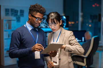 Poster - Two young interracial colleagues preparing presentation while scrolling through online information in tablet