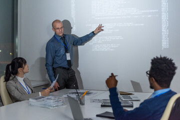 Poster - Mature coach pointing at interactive whiteboard while explaining data to young intercultural developers at seminar