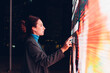 © Westend61 - Businesswoman with earphones using touch screen interactive information booth at night