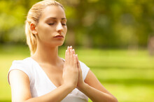 Beautiful Blond Woman With Hands Clasped Meditating At Park