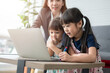 © Prot - Asian mother with her two grandchildren having fun and playing education games online with a digital computer laptop at home in the living room. Concept of online education and caring from parents.