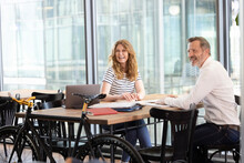 Happy Male And Female Professionals Looking Away While Sitting At Table In Office