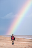 Fototapeta Tęcza - Rainbow over a beach with a man walking towards the rainbow