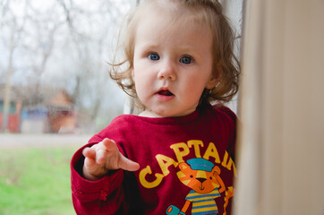 a little girl stands by the window and looks into the lens. girl