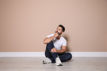 Wall Mural - Young man sitting on floor near beige wall indoors