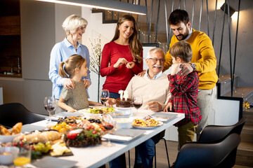 Family celebrating grandfather birthday with cake and candles at home