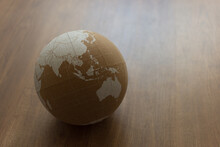 Cork World Ball With White Political Map On Brown Wooden Background Slightly Rotated And Shifted To The Left · Horizontal Frontal View