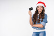 Smiling young caucasian teen girl in Christmas Santa Claus` hat holding credit card for New Year shopping, buying presents gifts, e-commerce isolated over white background