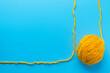Ball of yellow wool yarn on bright blue background. Knitting, handmade and hobby concept. Flat lay, top view with copy space.