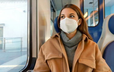 Wall Mural - Travel safely on public transport. Young woman with KN95 FFP2 face mask looking through train window. Commuter passenger with protective mask travels sitting on train.