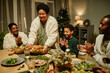 © Seventyfour - Portrait of smiling African-American grandmother bringing food to table while celebrating Thanksgiving with big happy family