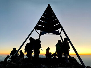 Toubkal National Park, Morocco, 26.10.2021. Silhouettes of happy hikers congratulating each other on top of Djebel Toubkal, North Africa's highest mountain, at sunrise. High Atlas Moiuntains, Morocco.