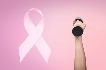 Wall Mural - First person raised woman's hand holding a dumbbell and pink ribbon, symbol of breast cancer awareness