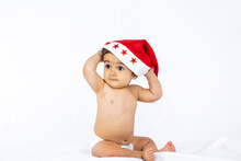 A Baby Boy With A Red Christmas Hat On A White Background, Copy Space, Taking Off The Santa Hat