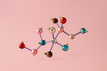 Colorful Christmas balls arranged in a chemical molecular structure. New Year's scientific minimal concept on pink background