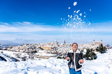 Blonde Woman With Braids Throwing Snow In The Air. Background Landscape Of The City Of Toledo Covered With Snow.