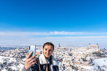 Blonde Woman With Braids Taking A Self Photo. Landscape Background Of The City Of Toledo Covered With Snow.