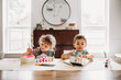 © Cavan Images - Young siblings sitting painting colorful boxes in modern dining room