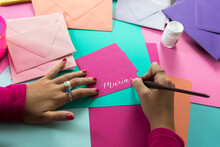 Hands Of Female Calligrapher Writing On Colorful Paper With White Ink