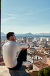 © Cavan Images - Man is sitting on a rooftop overlooking the city