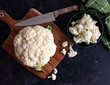 © Cavan Images - Cauliflower and florets on cutting board and in bowl on black counter.