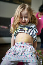 Cute Little Girl Artist Sitting On Chair Showing Her Pained Belly.