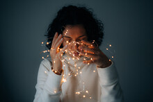 Woman With Curly Hair Holding String Lights On Dark Background