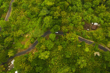 Top Down Overhead Aerial View Of A Car Driving On The Asphalt Road Through Lush Green Jungle Car On The Road Passing Rural House In The Rainforest In Bali, Indonesia