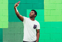 Black Afro American Boy On Green Background Taking A Selfie With His Mobile Phone.