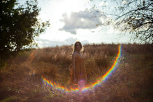 A Young Woman In A Dress Stands In A Hay Field With A Lens Flare Highlights Her Frame