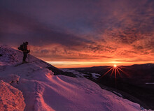 Skier Stands On Mountain In Winter With Stunning Red Pink Sunrise