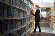 © Cavan Images - Young redhead girl with mask on in library looking at books.