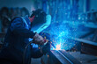© Cavan Images - Man with protective face and eye shield welding industrial steel beam