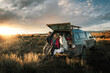 © Cavan Images - Cheerful couple sitting with dog at trunk of off-road vehicle on field during vacation